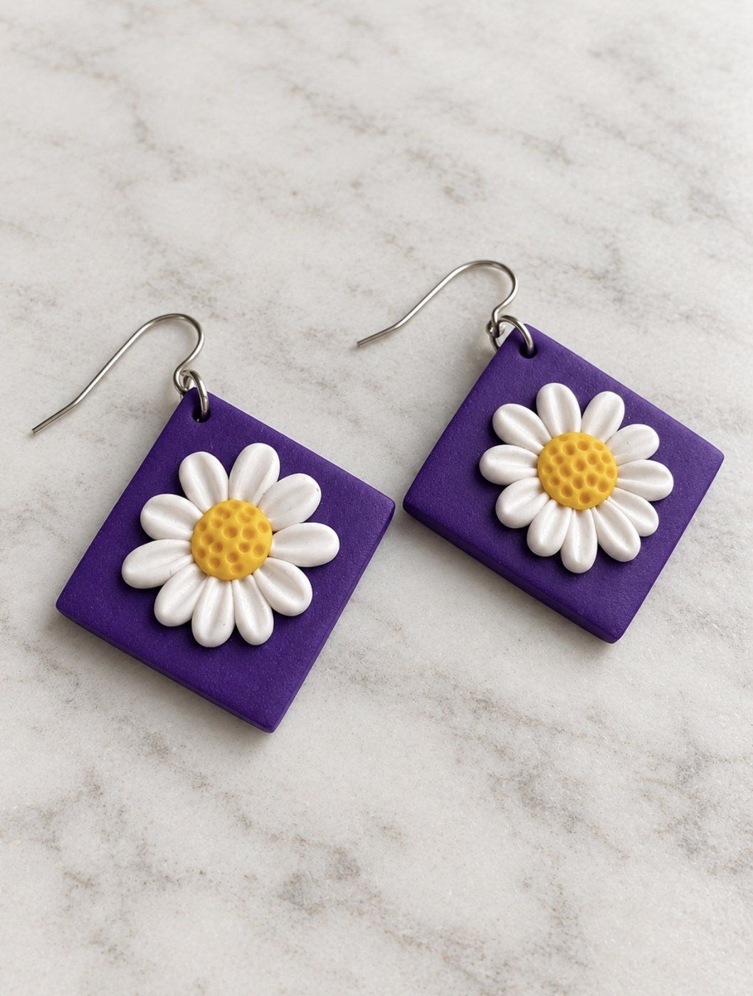 Aros cuadrados violeta con margarita blanca sobre mármol